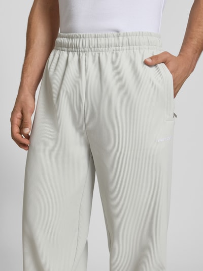Mężczyzna nosi Sweatpants mit Strukturmuster und elastischem Bund od Pegador, jasny materiał z fakturą, relaxed fit, elastyczny pas, materiał z domieszką stretchu, długość nogawki wewnętrznej 75 cm, zbliżenie na górną część spodni.