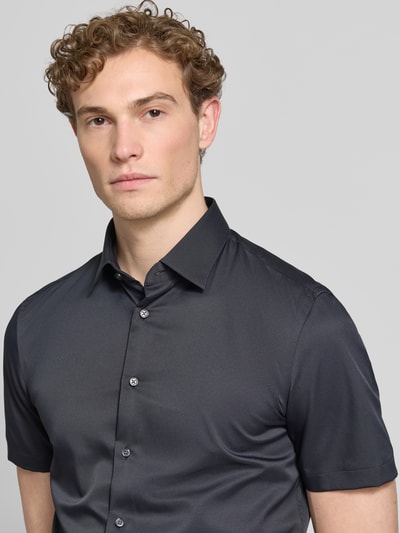 Männermodel trägt Slim Fit Business-Hemd mit Kentkragen van Jake*s in zwart, elastische materiaalmix, knoopsluiting, met korte mouwen, nahaufnahme bovenlichaam.