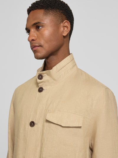 Męski model nosi Leinenjacke mit Stehkragen und Pattentaschen od bugatti, beżowy len, krój regular fit, zbliżenie na górną część ciała.