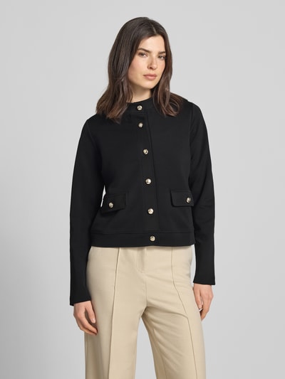 Frauenmodel trägt Kurzblazer mit Pattentaschen Modell 'Tasia' von JOOP!, schwarzer Baumwoll-Mix, goldener Knopfverschluss, Ganzkörperansicht von vorne.