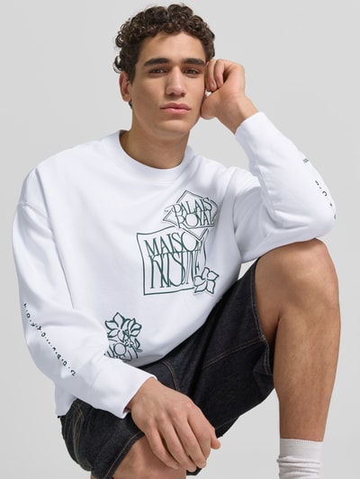 Männermodel trägt Oversized Sweatshirt aus Baumwoll-Mix von MAISON KITSUNÉ mit floraler Label-Stitching, weiß, elastische Abschlüsse, Nahaufnahme Oberkörper.