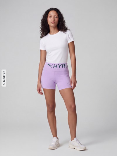 Frauenmodel trägt lilafarbene Skinny Fit Sportshorts mit Label-Print Modell 'PUMA x HYROX PWRMODE 4'' von PUMA, Damen Sportshorts von PUMA Performance, Ganzkörperansicht von vorne, KI-modifiziertes Bild.
