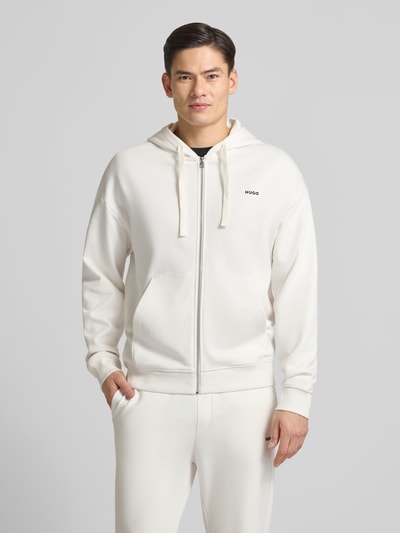 Männermodel trägt Relaxed Fit Sweatjacke aus reiner Baumwolle Modell 'DAPOZIP' von HUGO in Unifarbe mit Kapuze und Label Print, Ganzkörperansicht von vorne.