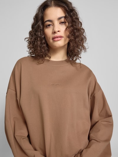 Frauenmodel trägt Regular Fit Sweater mit Logo-Stitching Modell 'Croissant' von OH APRIL in Braun, reine Baumwolle, Nahaufnahme Oberkörper.