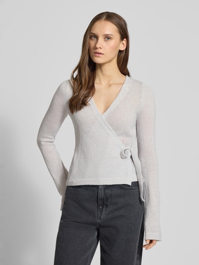 Frauenmodel trägt Strick-Cardigan in Wickeloptik von Review, hellgrau, Regular Fit, V-Ausschnitt, lange Ärmel, Schleifenverschluss, Nahaufnahme Oberkörper.