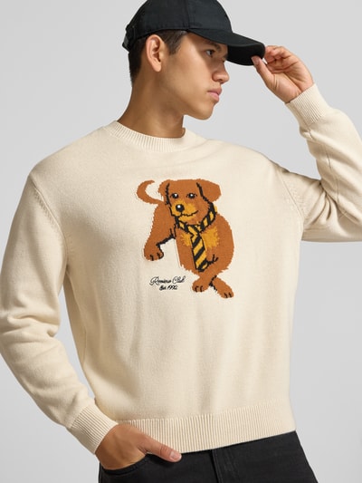 Männermodel trägt Relaxed Fit Strickpullover aus reiner Baumwolle von REVIEW, helle Farbe, Hundemotiv, gerippte Abschlüsse, Nahaufnahme Oberkörper.