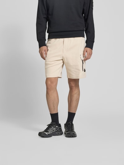 Männermodel trägt Shorts mit elastischem Bund von Moose Knuckles, Beige, reine Baumwolle, Cargo-Taschen, Straight Fit, Ganzkörperansicht von vorne.