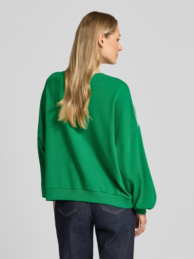 Frauenmodel trägt Oversized Sweatshirt aus Baumwoll-Mix Modell 'JAMIE' von Vero Moda in Grün mit Kontraststreifen, unifarben, Ganzkörperansicht Rückansicht.