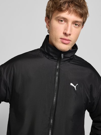 Mężczyznamodel nosi Sherpa Jacket mit Reißverschluss od PUMA PERFORMANCE, kolor czarny, stójka, zamek błyskawiczny, nadruk z logo, luźny krój, kieszenie zapinane na zamek błyskawiczny, długość tyłu 68 cm, szerokość ramion 60 cm, szerokość klatki piersiowej 63 cm, długość rękawów 59 cm. Nahaufnahme górnej części ciała.