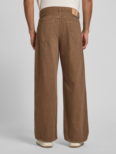 Męski model nosi Jeans mit Eingrifftaschen Modell 'Type 3' od Wood Wood, bawełna, krój relaxed fit, szerokość w rozmiarze 32/32: 44 cm, długość wewnętrzna nogawki: 75 cm, brązowy kolor, widok całej sylwetki z tyłu.