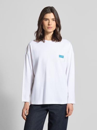 Vrouwenmodel draagt Longsleeve met Label-Print model 'GIXY' van American Vintage in wit, relaxed fit, ronde hals, katoenen textuur, voorkant bovenlichaam close-up.