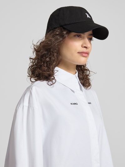 Frauenmodel trägt Relaxed Fit Hemdbluse mit Logo-Stitching von Karo Kauer in Weiß aus reiner Baumwolle, Hemdblusenkragen, Langärmelig, durchgängige Knopfleiste, Rückenlänge bei Größe S 79 cm, Ärmellänge 63 cm; Nahaufnahme Oberkörper.
