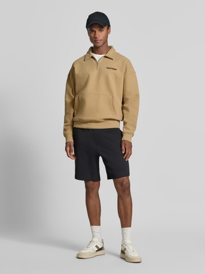 Mannelijk model draagt regular fit schipperstrui uit katoenmix van Polo Ralph Lauren in beige, zwarte shorts en witte sneakers, ganzebody vooraanzicht.