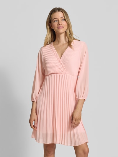 Frauenmodel trägt knielanges Kleid mit Plisseefalten Modell 'Im44sa' von ZABAIONE in zartem Rosa, Wickel-Optik, Nahaufnahme Oberkörper.
