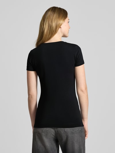 Vrouwenmodel draagt 'Slim Fit T-Shirt met Strasssteinbesatz' van Guess in zwart, elastisch katoenmix, logo detail, slim fit, ronde hals. Volledige lichaamsweergave achteraan.