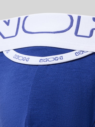 Mannenmodel draagt String met elastische band van WOH, mix van katoen en elastaan, nauwsluitende pasvorm, labeldetails. Detailopname.