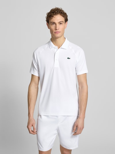 Męski model ma na sobie Regular Fit Sport Poloshirt mit Label Patch od Lacoste Sport, biała pikowana tkanina, widok całej sylwetki z przodu.