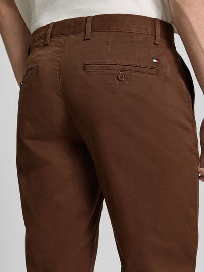 Mężczyzna nosi Slim Fit Chino aus Baumwoll-Mix od Tommy Hilfiger, bawełniany materiał, jednolity kolor, kieszenie z guzikami, detal logo, detaliczne ujęcie tylnej części.
