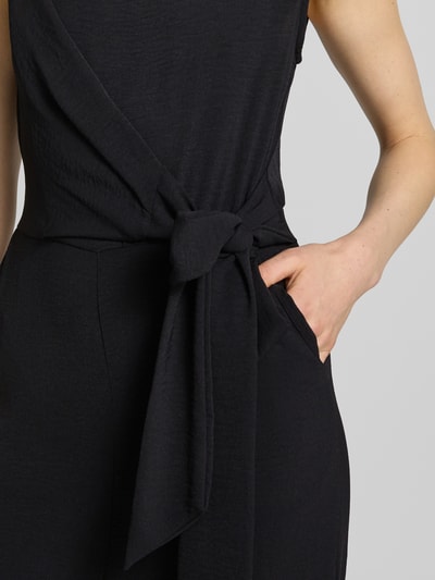 Frauenmodel trägt Jumpsuit mit Bindegürtel Modell 'Jessica' von GUIDO MARIA KRETSCHMER WOMAN in Schwarz, Wickel-Optik, Nahaufnahme Oberkörper, taillierter Schnitt, U-Boot-Ausschnitt, Rückseitiger Reißverschluss, strukturierte Stofftextur, Kontext: Rückenlänge 36 cm, Brustweite 38 cm, Gesamtlänge 148 cm, Innenbeinlänge 77 cm bei Größe 36.