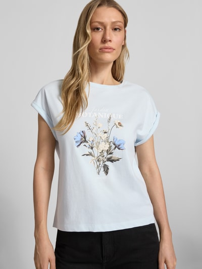 Modelka nosi damski t-shirt Relaxed Fit T-Shirt aus reiner Baumwolle von s.Oliver RED LABEL, efekt: jednolity kolor, krój relaxed fit, nadruk z przodu, nadruk z logo, ramiona obniżone, okrągły dekolt, krótki rękaw z brzegiem, materiał: bawełna; jasne kolory, motyw kwiatowy; zbliżenie na górną część ciała, widok z przodu.