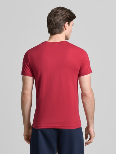 Männermodel trägt T-Shirt mit Label-Detail van Gant in rood, puur katoen, recht model, ronde hals, ruglengte maat M 70 cm, Ganzkörperansicht Rückansicht.