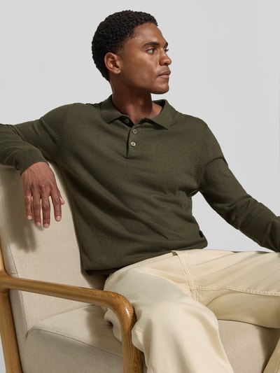 Mężczyznamodel nosi Regular Fit Strickpullover aus Baumwoll-Mix mit Kaschmir-Anteil von Casual Friday, mieszanka bawełny i kaszmiru, kołnierzyk polo, elastyczne wykończenia, długość tyłu w rozmiarze M 65 cm, długość rękawów 69 cm, kolor oliwkowy i jasnokremowe spodnie, tło jasnoszare. Ujęcie: całe ciało od przodu.