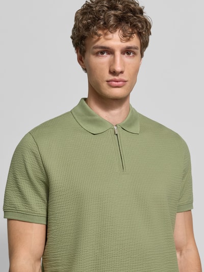 Męski model nosi Regular Fit Poloshirt mit Strukturmuster von MCNEAL, mieszanka bawełny, zamek błyskawiczny, krótki rękaw, kolor jasna zieleń, fakturowany wzór, długość tyłu 70 cm w rozmiarze M, zbliżenie górnej części ciała.