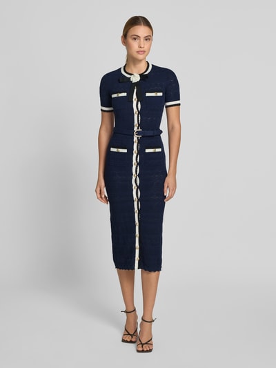 Frauenmodel trägt Slim Fit Midikleid in Strick-Optik von Self-Portrait aus dunkelblauem Baumwoll-Mix mit durchgängiger Knopfleiste, Weiß-Details, Kurzärmelig, Gesamtlänge 126 cm, Brustweite 41 cm, Ärmellänge 23 cm, Taillenweite 34 cm, Ganzkörperansicht von vorne.