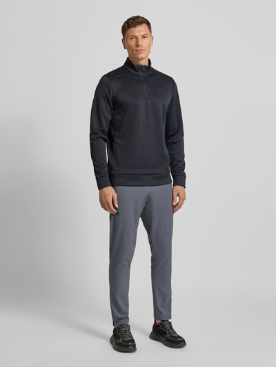 Męski model nosi szare spodnie treningowe z zamykanymi kieszeniami Vanish Woven Tapered Pant od Under Armour, regular fit, widok z przodu.