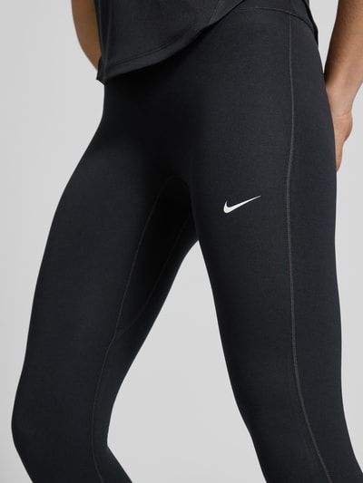 Frauenmodel trägt schwarze Leggings mit Logo-Print Modell 'One' von NIKE TRAINING aus Material-Mix mit Stretch-Anteil, Nahaufnahme Oberkörper.