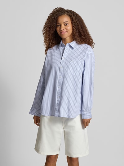 Vrouwenmodel draagt Relaxed Fit blouse met labelstitching Model 'Keene' van Carhartt Work In Progress, puur katoen, overhemdkraag, knoopsluiting, borstzak, witte en blauwe strepen, gladde textuur, ruglengte maat S 78 cm, mouwlengte maat S 56 cm, frontale volledige lichaamsperspectief.