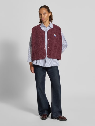 Frauenmodel trägt Regular Fit Weste aus Teddyfell Modell 'Hoktown' von American Vintage in Bordeaux, strukturierte Oberfläche, Knopfleiste, Logo-Patch, Ganzkörperansicht von vorne, Damen Weste, Teddyfell Regular Fit, Rückenlänge 57 cm, Schulterbreite 43 cm, Brustweite 63 cm.