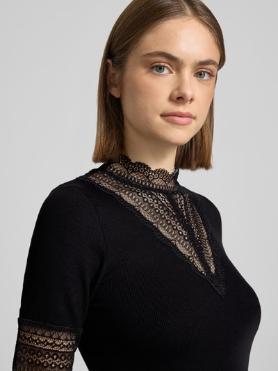Vrouwenmodel draagt Slim Fit T-Shirt uit viscosemix model 'Tilde' van Only, uni zwart, met kantdetails, fijnribstructuur, rondhals, korte mouw, close-up bovenlichaam.