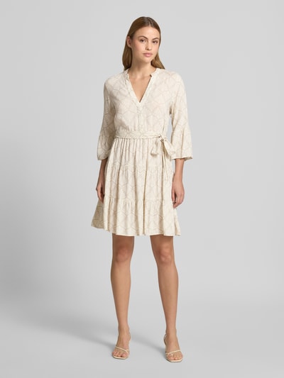 Frauenmodel trägt Tailliertes Tunikakleid aus reiner Viskose Modell 'MELBA' von Vero Moda, Optik:Allover-Muster, Mini, V-Ausschnitt, Gürtelschlaufen, Bindegürtel, Trompetenärmel, Volant-Saum, Material: reine Viskose, helle Farbgebung, weiche Textur, Ganzkörperansicht von vorne.