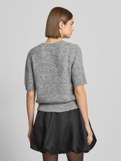 Frauenmodel trägt Strickpullover mit 1/2-Arm und Rundhalsausschnitt von Gina Tricot im grauen Material-Mix mit Lanawoll-Anteil, Regular-Fit, Ziersteinbesatz, kombiniert mit schwarzem Rock, Rückenlänge bei Größe S 53 cm, Ärmellänge 28 cm, Ganzkörperansicht Rückansicht.