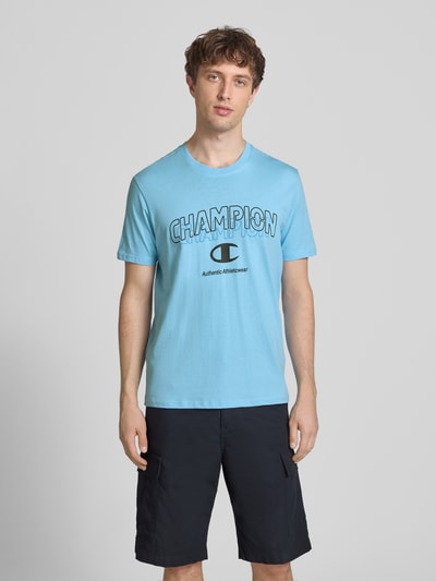 Männermodel trägt T-Shirt mit Label-Print und Rundhalsausschnitt von CHAMPION in Hellblau, Regular-Fit, Reine Baumwolle, Ganzkörperansicht von vorne. Rückenlänge in Größe M: 68 cm.