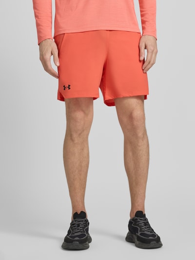 Męski model nosi Straight Fit Shorts mit Logo-Print Modell 'Vanish' od Under Armour, kolor pomarańczowy, elastyczny pas, kieszenie boczne, szerokość w rozmiarze M: 38 cm, długość nogawki od wewnątrz w rozmiarze M: 15 cm, krój straight fit, widok całej sylwetki z przodu.