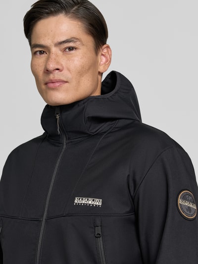 Männermodel trägt Regular Fit Jacke mit Logo-Print von Napapijri in Schwarz, glatte Textur, Reißverschluss, Nahaufnahme Oberkörper. Kontext: Herren Jacke mit Stehkragen, Eingrifftaschen mit Reißverschluss, elastische Abschlüsse, Maße bei Größe M: Rückenlänge 69 cm, Schulterbreite 52 cm, Brustweite 60 cm, Ärmellänge 68 cm.