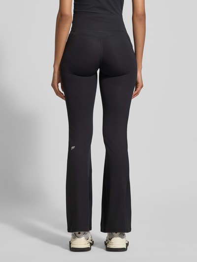 Frauenmodel trägt schwarze Flared Fit Leggins mit Logo-Print Modell 'OASIS' von Fabletics, elastischer Material-Mix, Ganzkörperansicht Rückansicht.