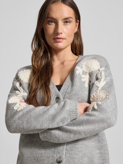 Frauenmodel trägt Strickjacke mit Knopfleiste von More & More in Grau, Material-Mix, V-Ausschnitt, gerippte Abschlüsse, Nahaufnahme Oberkörper.