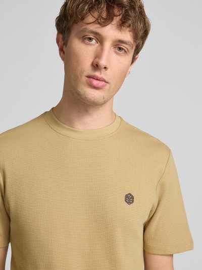 Męski model nosi t-shirt z bawełny o prostym kroju, model 'FILLIP' z detalem z logo od Blend, okrągły dekolt, długość tyłu 69 cm w rozmiarze M, zbliżenie na górną część ciała.