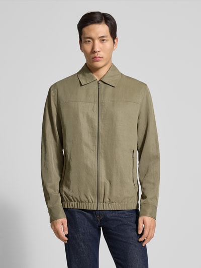 Männermodel trägt Regular Fit Jacke aus Lyocell-Mix von Guess in Olivgrün mit Umlegekragen, Reißverschlusstaschen, Ganzkörperansicht von vorne.