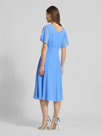 Modelka nosi Knielanges Kleid mit Rundhalsausschnitt od Vera Mont, półprzezroczysty materiał, taliowany krój, wszyty zamek błyskawiczny, okrągły dekolt, krótki rękaw, halka pod spódnicę, długość tyłu w rozmiarze 36: 102 cm, szerokość klatki piersiowej w rozmiarze 36: 37 cm, długość rękawów w rozmiarze 36: 27 cm, jasnoniebieski kolor, lejące tkaniny, gładka tekstura, widok całej sylwetki z tyłu.