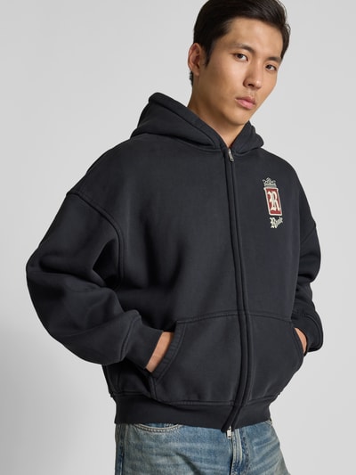 Männermodel trägt Oversized Sweatjacke aus Baumwolle von RHUDE in Schwarz mit Zweiwege-Reißverschluss, Känguru-Tasche, überschnittenen Schultern, reine Baumwolle, Rückenlänge 65 cm, Schulterbreite 60 cm, Ärmellänge 56 cm, Nahaufnahme Oberkörper.