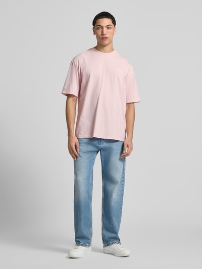 Męski model nosi Oversized T-Shirt aus reiner Baumwolle Modell 'Pike' von Pegador w jasnoróżowym kolorze, okrągły dekolt, haft z logo, półrękaw, kontekst: męska koszulka, 100% bawełna, oversize, długość tyłu w rozmiarze M: 71 cm, widok całej sylwetki z przodu