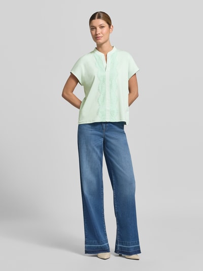 Frauenmodel trägt Regular Fit Bluse aus Baumwoll-Mix mit Spitzenbesatz von Marc Cain in Hellgrün, kombiniert mit blauer Jeans, Ganzkörperansicht von vorne.