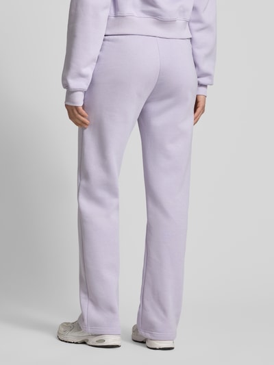 Männermodel trägt spodnie dresowe z mieszanki bawełny, krój relaxed fit Modell 'Iconic' od Gina Tricot, elastyczny pas, tunel, długość wewnętrzna nogawki w rozmiarze S 80 cm, jasnofioletowe, gładka faktura, całkowity widok z tyłu.