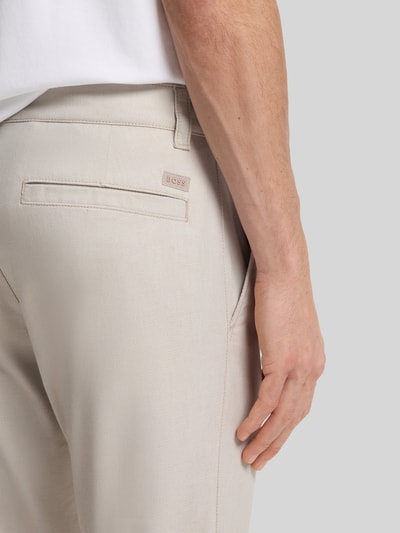 Männermodel trägt Slim Fit Chino aus Baumwoll-Mix mit Leinen und Viskose-Anteil von BOSS Orange in heller Farbe, Label-Patch, Nahaufnahme Rückansicht. Denim-Optik, Passform Slim Fit, Mid Waist, seitliche Eingrifftaschen, Gesäßtaschen, Materialverarbeitung Twill.