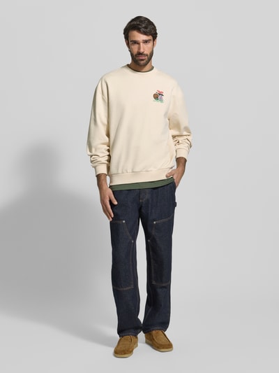 Męski model nosi Sweatshirt mit Label-Print und Rundhalsausschnitt od Les Deux, jasny krem, luźny krój, bawełna, widok całej sylwetki z przodu.