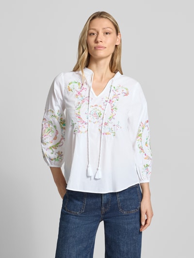 Frauenmodel trägt Bluse mit Schlüsselloch-Ausschnitt und Schnürung von Emily Van den Bergh aus Reine Baumwolle mit 3/4-Arm, Straight Fit, elastische Ärmelabschlüsse, abgerundeter Saum, weiß mit pastellfarbenem Print, Ganzkörperansicht von vorne. Rückenlänge bei Größe 36: 62 cm, Ärmellänge bei Größe 36: 50 cm.